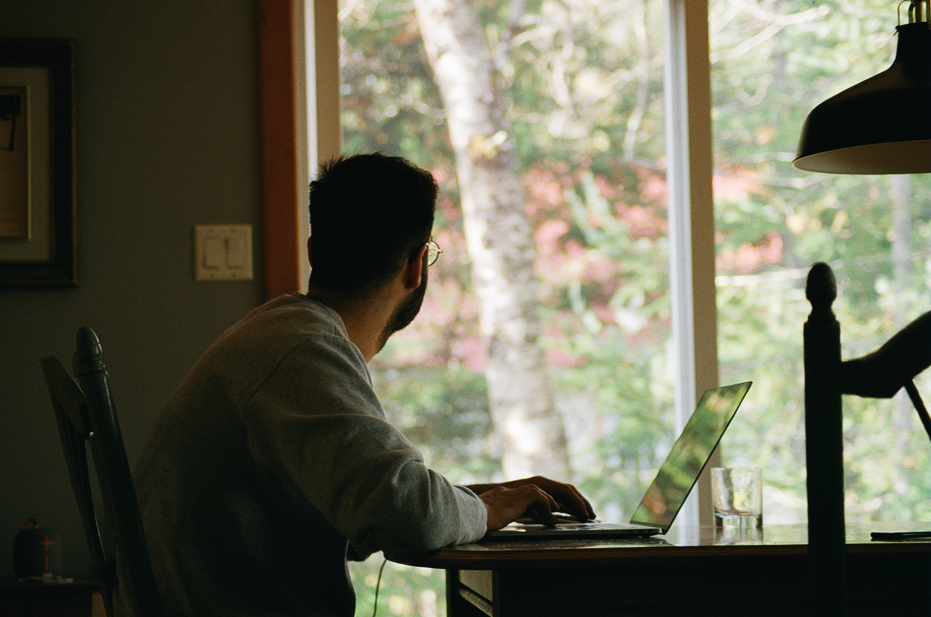 Person wearing glasses working from their desk indoors but staring outside the glass doors